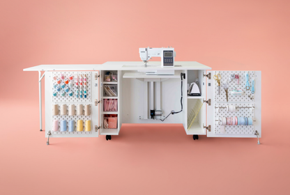 Sewing machine with open cabinet doors displaying various sewing supplies on a pink background [Deluxe]