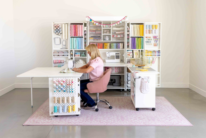Person sitting at a desk in a home office with shelves filled with supplies [Deluxe]